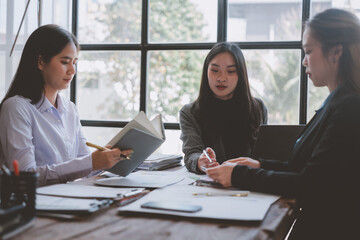 Three young businesswomen are having a productive meeting in a modern office, collaborating on a project and reviewing documents at a wooden table