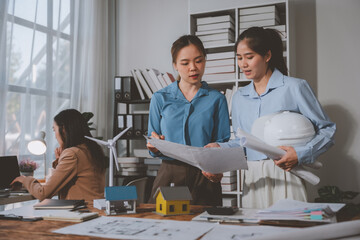 Two female architects are examining blueprints and discussing a sustainable building project in their office, showcasing teamwork and expertise in green architecture