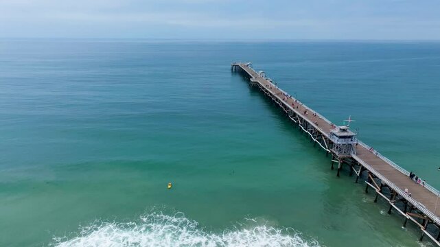 Surfer on yellow surfboard catching wave next to San Clemente pier