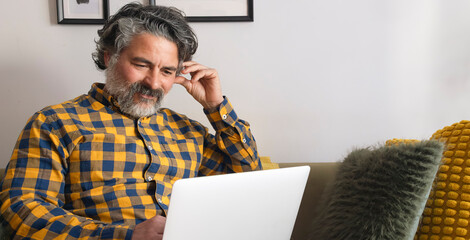 Smiling mature man using laptop on sofa at home