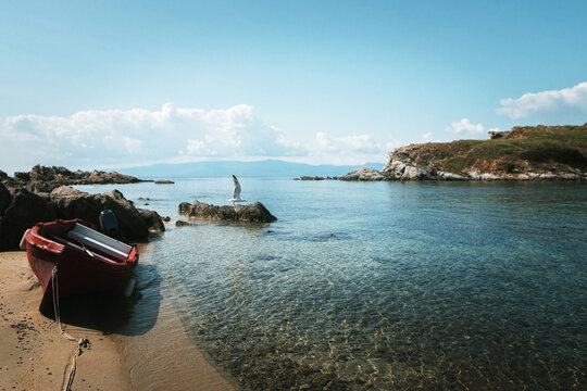 Serene Coastal Scene with Red Boat and Rocky Outcrops