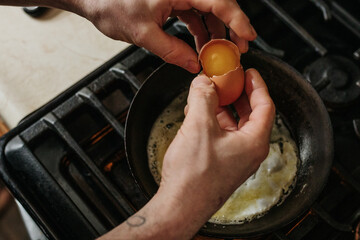 Overhead view of man cracking egg into hot pan on gas stove