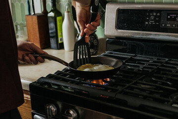 wide shot of a man cooking eggs for breakfast on his gas stove