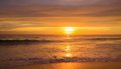 Obraz premium A golden sunset over the ocean, with gentle waves washing onto the shore, creating a peaceful and serene atmosphere.