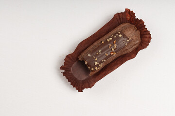 A chocolate ?clair with a glossy ganache topping and crushed nuts, placed in a brown wrapper on a...
