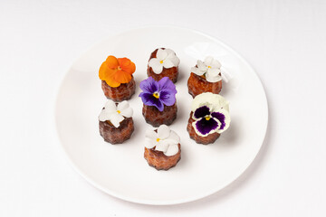 A plate of golden-brown canel?s, beautifully adorned with colorful edible flowers, presented on a white table setting.