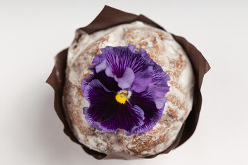 Close-up of a muffin with a generous dusting of powdered sugar and a striking deep purple edible flower on top.