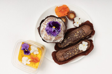 A carefully arranged plate of desserts, including chocolate ?clairs and a sugar-dusted muffin, beautifully garnished with vibrant edible flowers.