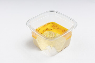 A close-up of a plastic container with a yellow mango-flavored dessert topped with small seeds.