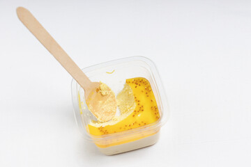 A plastic container with a partially eaten mango-flavored dessert and a wooden spoon inside.