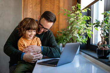 Fatherhood and remote business. Happy young single dad working at home while child plays next to him