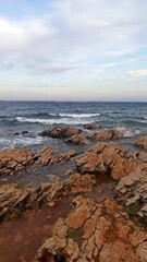 Obraz premium Rocky Coastal Seascape in Croatia with Waves Crashing Against Reddish Rocks Under a Cloudy Sky at Sunset, Natural Sea Landscapes
