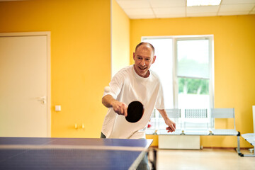 A man in a white T-shirt enjoys playing table tennis. Friendly compete in ping pong club