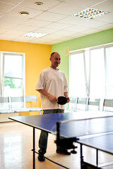A man in a white T-shirt enjoys playing table tennis. Friendly compete in ping pong club