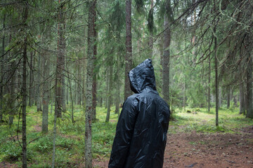 A man's back wearing a black raincoat standing alone in the middle of the forest in rainy weather	