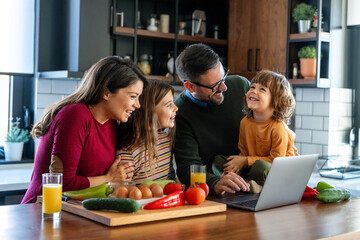 Happy young family with kids in kitchen have fun using modern laptop together, enjoying weekend