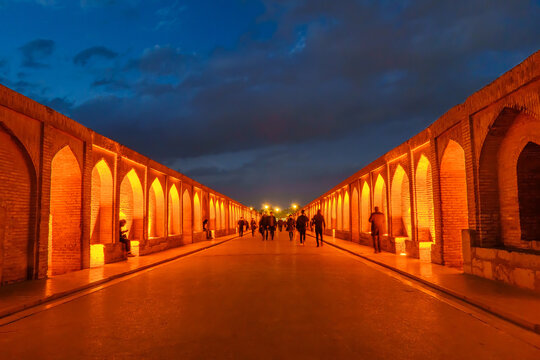 Allahverdi Khan Bridge, also known as Si-o-se-pol, Isfahan, Iran. View from the walking section of the bridge at night. Blurred silhouettes of walking locals and tourists are visible