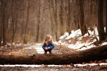 Cute young girl sitting on tree stump in snowy forest