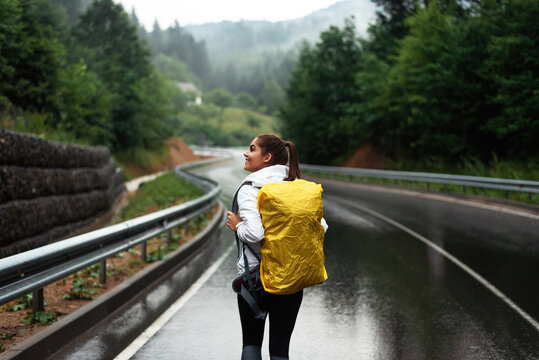 Young woman with backpack walking alone among rainy mountains