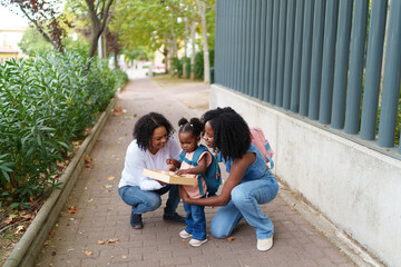 Two mothers helping their daughter with alphabet puzzle on sidewalk