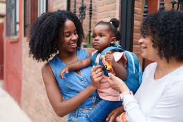 Mother holding her smiling daughter ready for kindergarten with grandmother