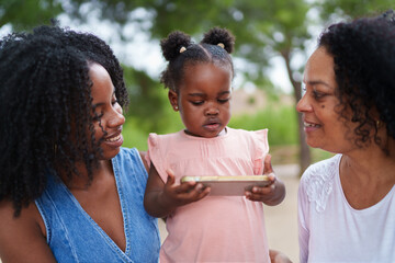 Little girl using smartphone with mother and grandmother outdoors