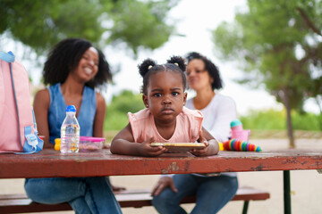 Little girl using tablet at park with family watching