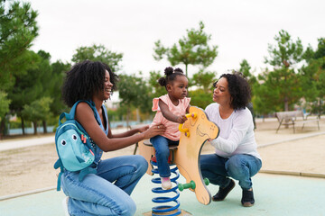 Happy family playing at the playground with baby girl riding a rocking horse