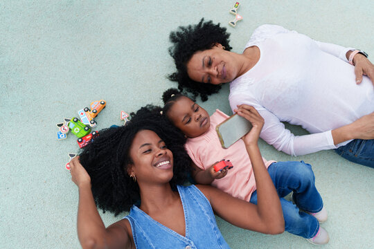 Three generations of black women relaxing and playing with toys and smartphone