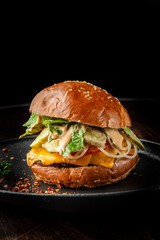 A delicious cheeseburger on a black plate, featuring a sesame seed bun, melted cheddar cheese, lettuce, pickles, and a creamy sauce, set against a dark background.
