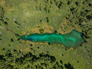 A hidden and mysterious lake hidden in the Altai mountain forest. Lake in the forest in the form of a drop, view from a quadcopter. The emerald lake photographed from above by a drone.