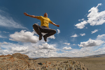 A man in bright clothes jumps into the air and freezes in a cheerful pose with a view of the sky. Funny pose while jumping with open arms against the background of nature.