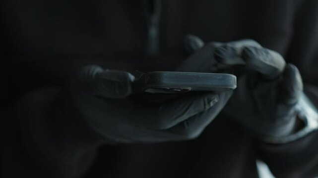 A scammer in black gloves enters a PIN code on the phone.
A man is trying to unlock his mobile phone.
Thief with a phone in his hands.
Black latex gloves and a phone in hands, close-up