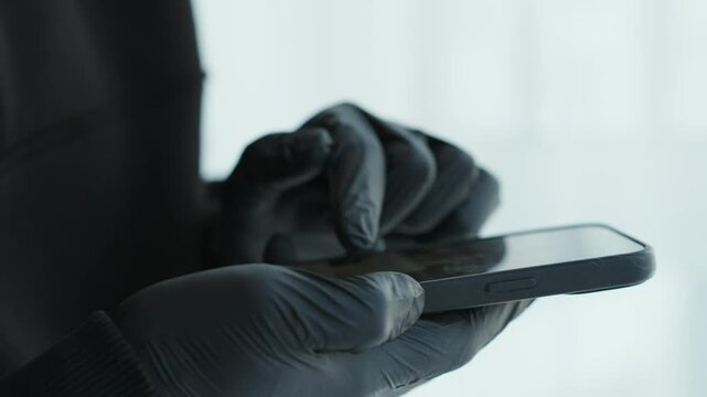 A scammer in black gloves enters a PIN code on the phone.
A man is trying to unlock his mobile phone.
Thief with a phone in his hands.
Black latex gloves and a phone in hands, close-up