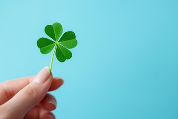 Close-up of a woman’s hand holding a green four-leaf clover on a blue background, representing the luck and joy of St. Patrick’s Day, with space available for adding your personal holiday message.