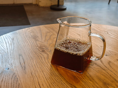 Coffee Pot with Black Filter Coffee and Beans: A glass pot filled with freshly brewed black coffee, placed on a wooden table.