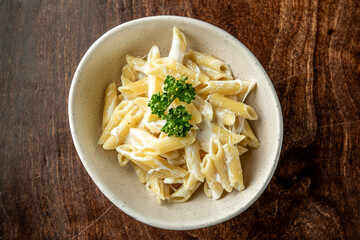 A bowl of creamy penne pasta garnished with fresh parsley, presented on a wooden surface. The dish showcases a smooth, rich sauce that enhances its appetizing appearance.