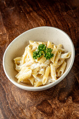 A bowl of creamy penne pasta garnished with fresh parsley, presented on a wooden surface. The dish showcases a smooth, rich sauce that enhances its appetizing appearance.