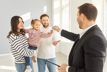 Professional male realtor giving house key to a young happy smiling family with cute little child...
