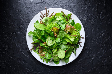 White plate filled with mix of fresh salad greens on black background. Top view food photography