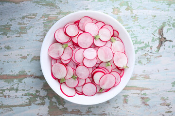 A white plate filled with thin radish slices on rustic wooden table. Vegetable salad. Food photography