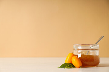 Kumquat and jar of jam on beige background, space for text