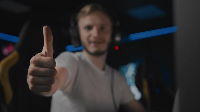 Adult gamer gives a thumbs up, positive assessment gesture. Professional gamer playing multiplayer online battle arena game on PC at cyberspace club. Real-time strategy, first-person shooter game
