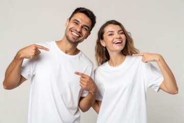 Obraz premium Young Man and Woman Smiling and Pointing at Each Other in Plain White Tees on Neutral Background