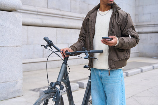 Young man holding his bicycle and using mobile phone in the city