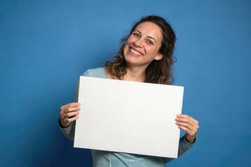 Naklejka premium A Joyful Woman Holding a Blank Sign Against a Vibrant Blue Background in a Studio Setting