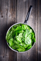 Freshly washed green spinach leaves in a metal colander on rustic wooden table. Raw organic baby...