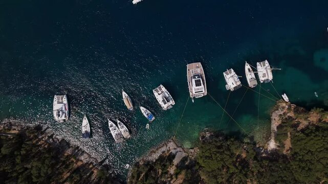 Top down aerial establishing of boats moored near Foki Beach, Kefalonia, Greece, in clear blue waters, anchored lines out to rocks