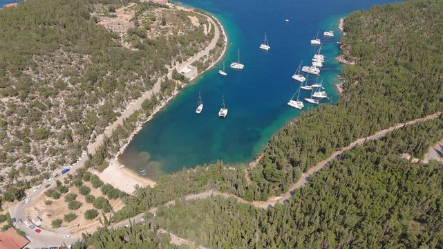 Drone pullback Foki Beach, Kefalonia, Greece, boats floating near the forested coastline