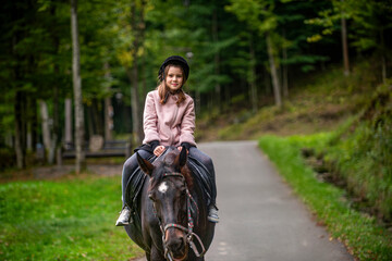 Little girl riding a horse at summer. Child girl rides horse on the outdoors in the middle of the...